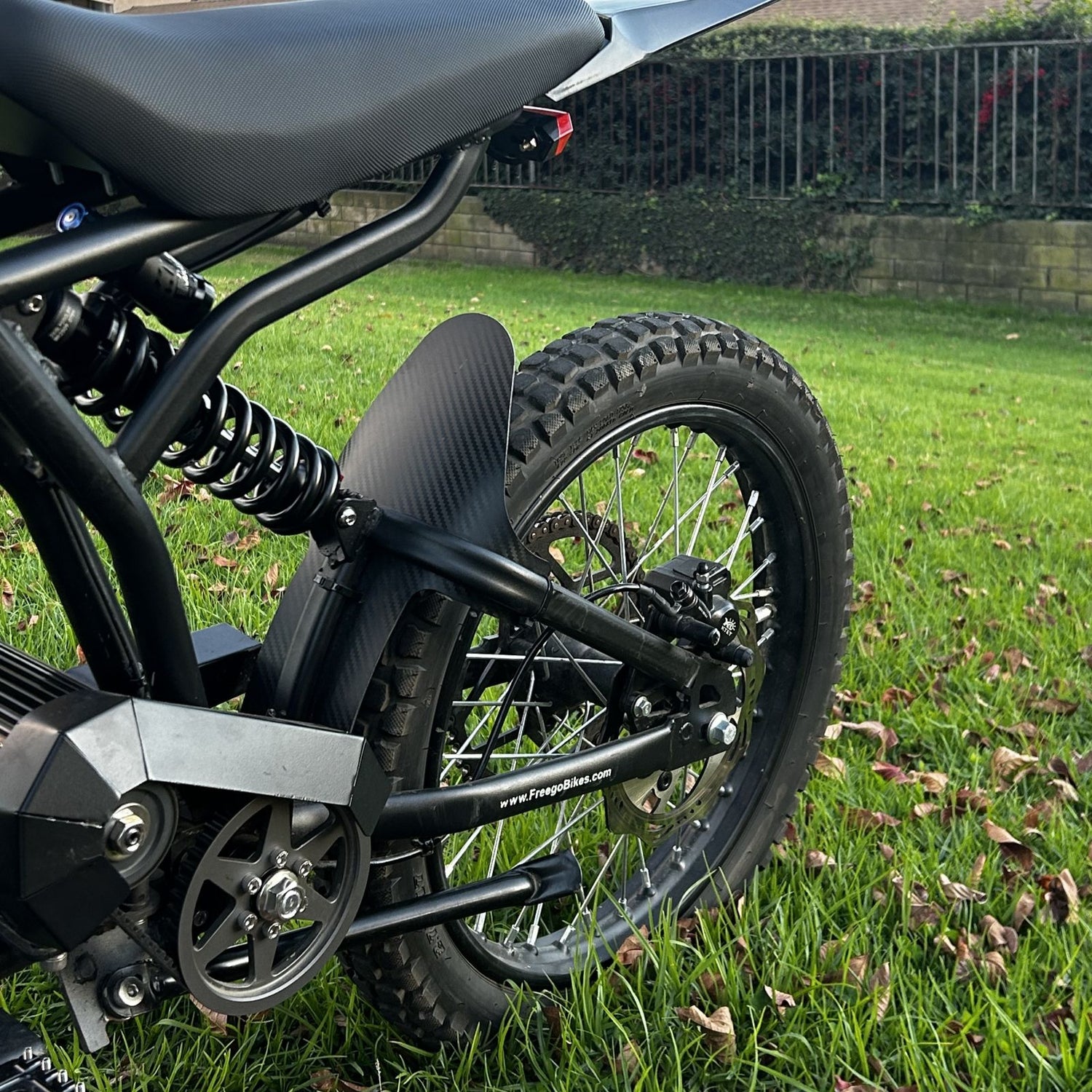 Rear view of the Freego Nova 3 electric off-road bike featuring thick knobby tires, dual coil spring suspension, padded seat, and rear fender, parked on a grassy lawn.