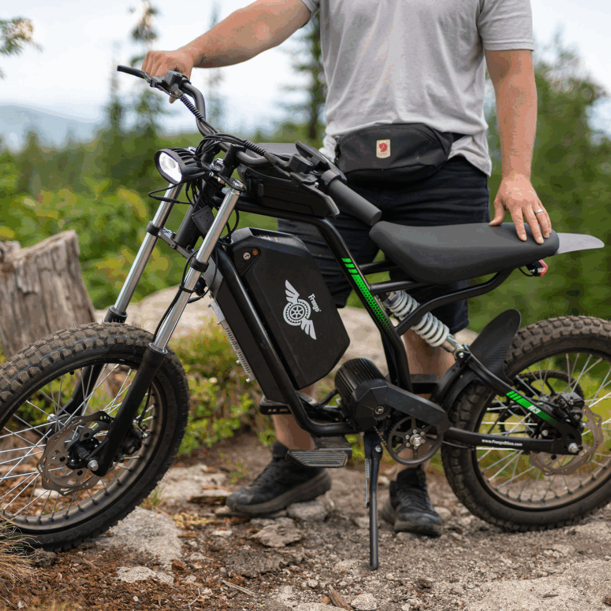 Person standing next to a Nova 3 ebike on a trail with greenery in the background
